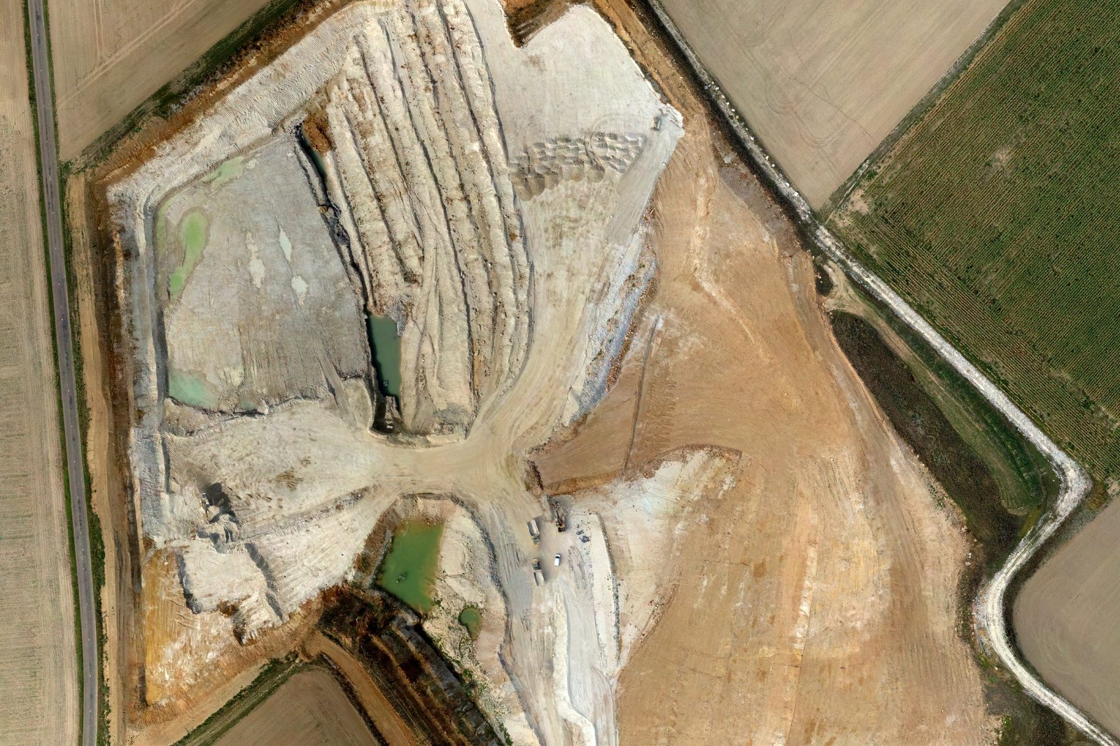 Vue verticale par drone d'une carrière en fosse : fronts de taille, gradins, pistes, fond de fouille en eau et terres de découverte