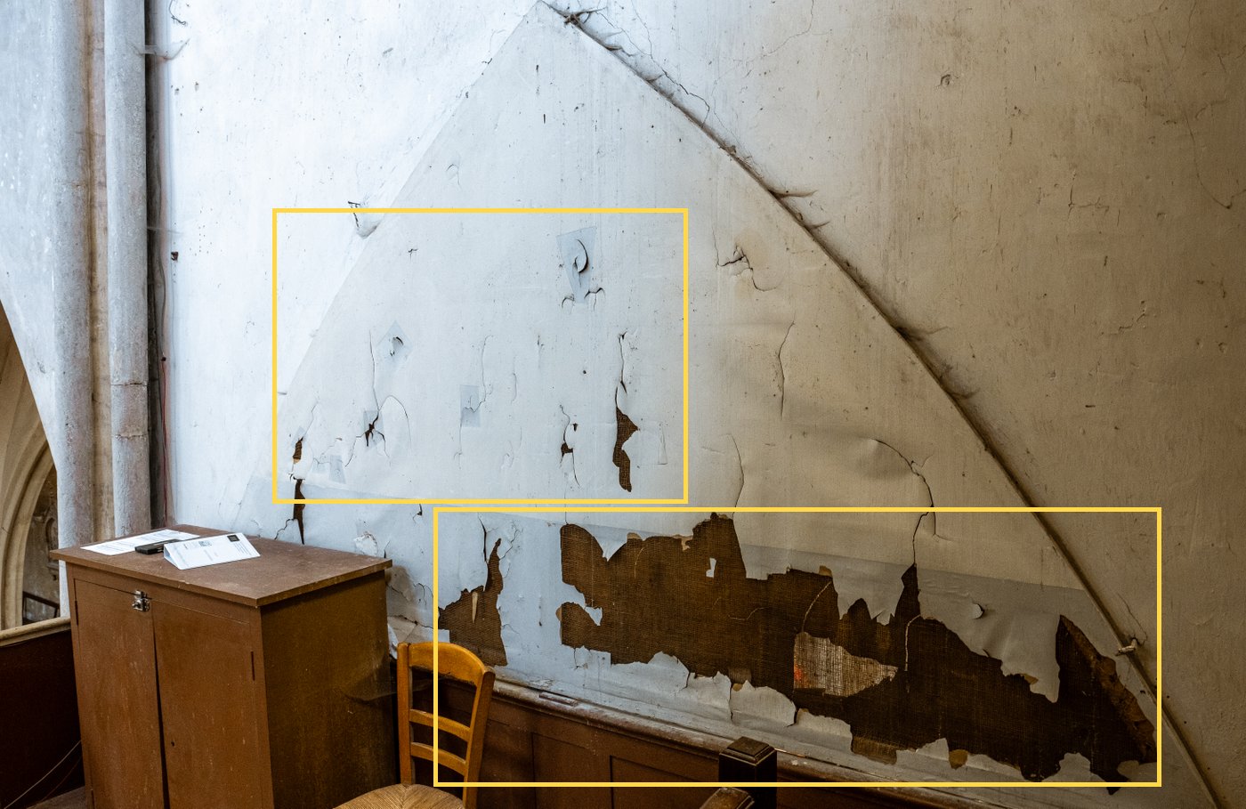 Paint flaking off in sheets at the bottom of a wall under a vault