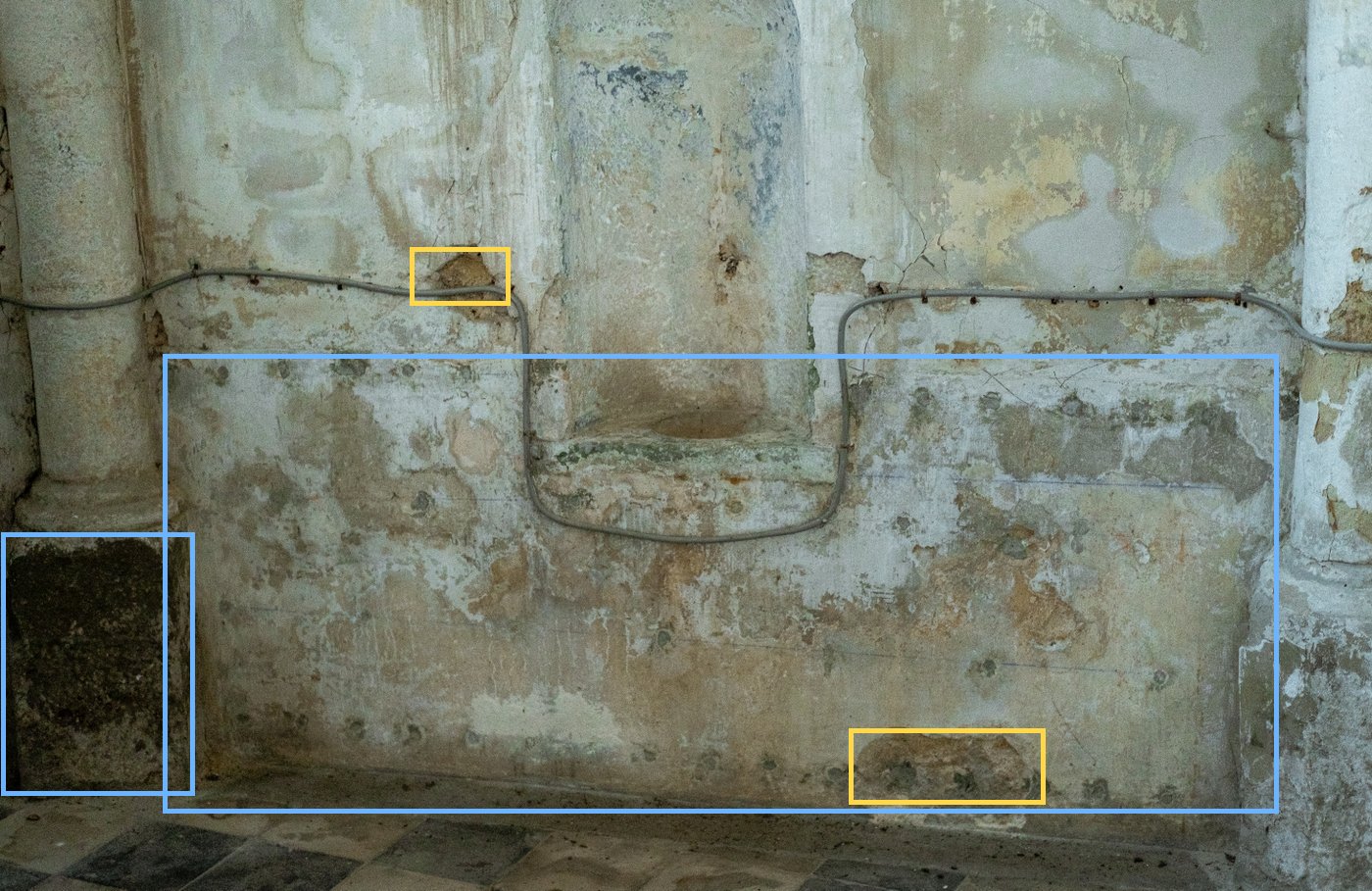 Damp wall base: mottled plaster, missing patches and wet stone at the foot of a column